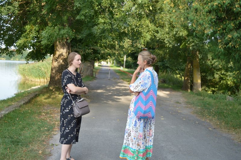 Two women stand outside on a road taking to each other