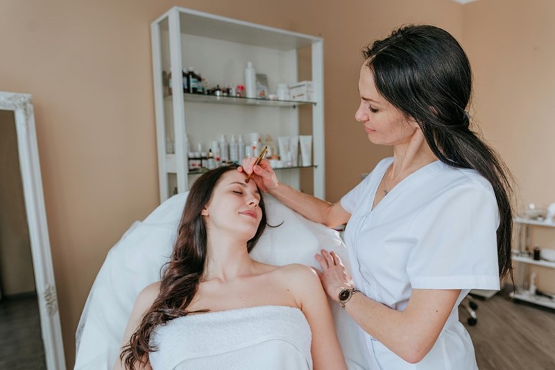 Esthetician treating a client at a med spa, the type of work the employee’s former employer still needed her to perform after laying her off.