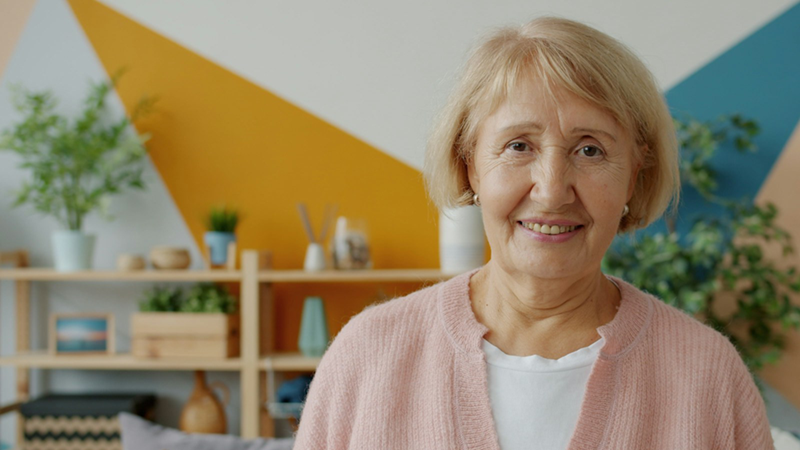 An older woman smiles with shelves in the background.