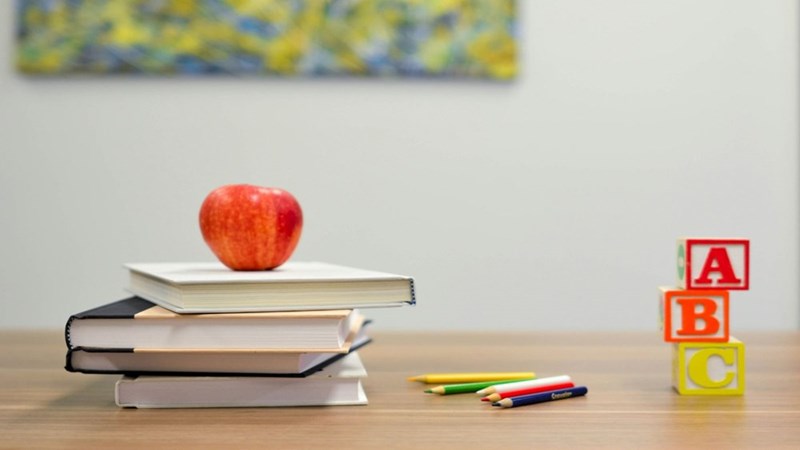 A table with books, toys, pencils and an apple.