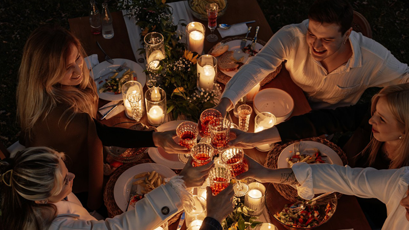 A group of friends raising a toast across a candlelit dinner table at night.