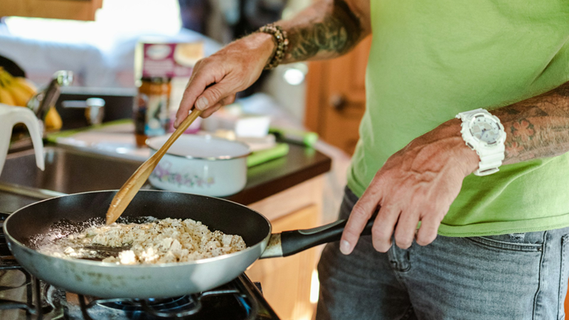 Close-up of a man cooking food on a stove.