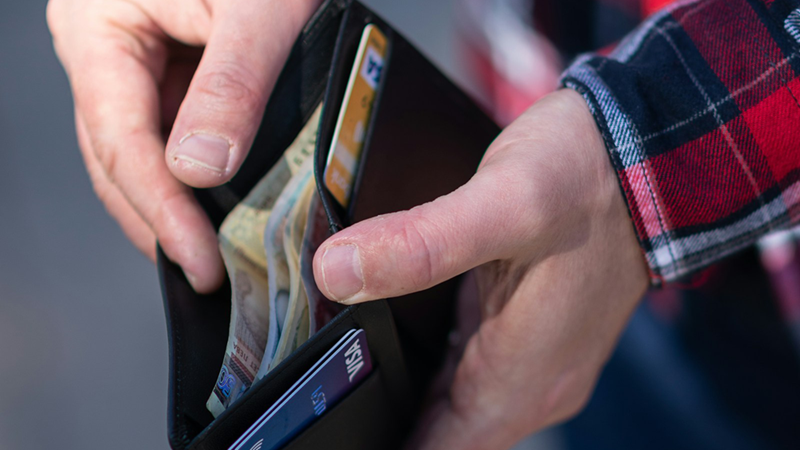 A man's hands open a black wallet with cards and cash inside.