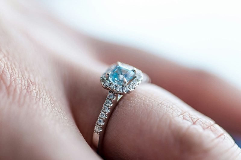An engagement ring with a precious gemstone sits on someone's finger