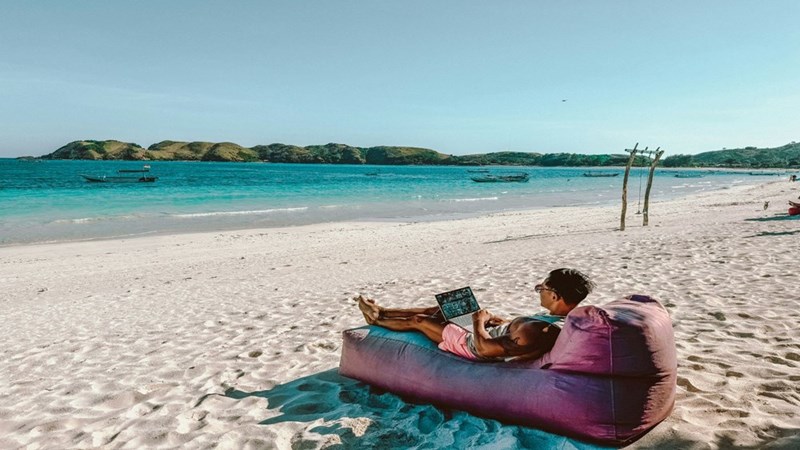 An employee working remotely from a beach with his computer. Not actual story subjects.