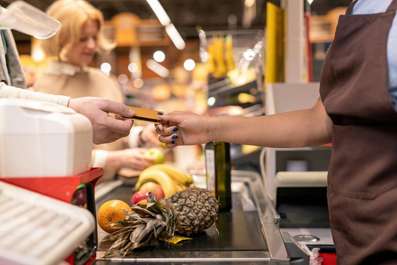 A man giving the cashier the credit card that his girlfriend blocked him from using until he cleaned up his trash.
