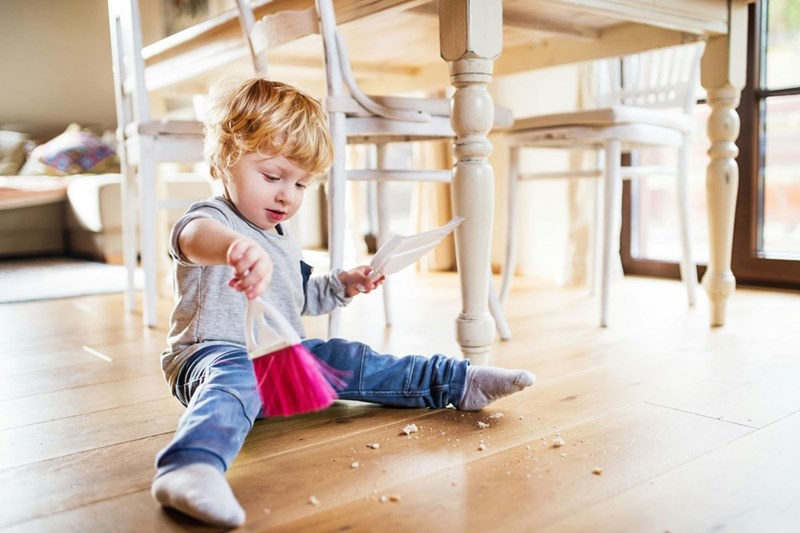A toddler cleaning up after himself with a broom and pan.