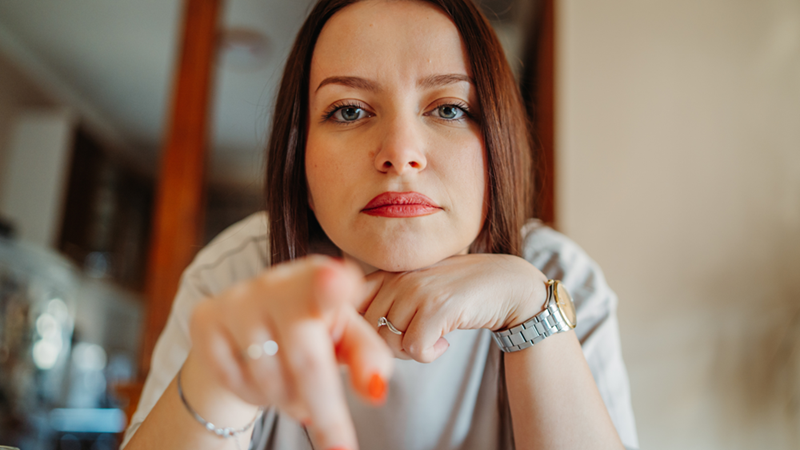 Woman resting her chin on one hand and points with the other like she'd reading something with extra focus