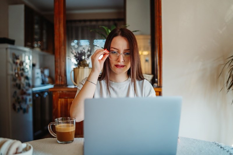 Woman sitting with a laptop adjusting her glasses, like she's reviewing somthing improtant