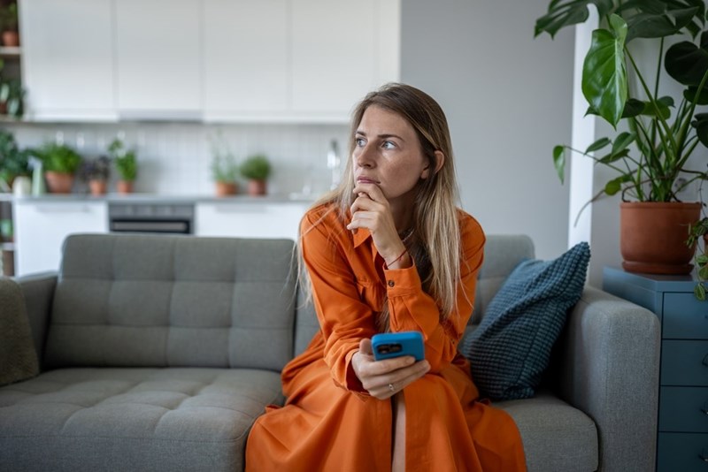 woman in orange dress sittng on a couch with a concered look
