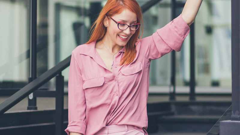 A female employee smiles and raises her arm while walking down stairs outside.