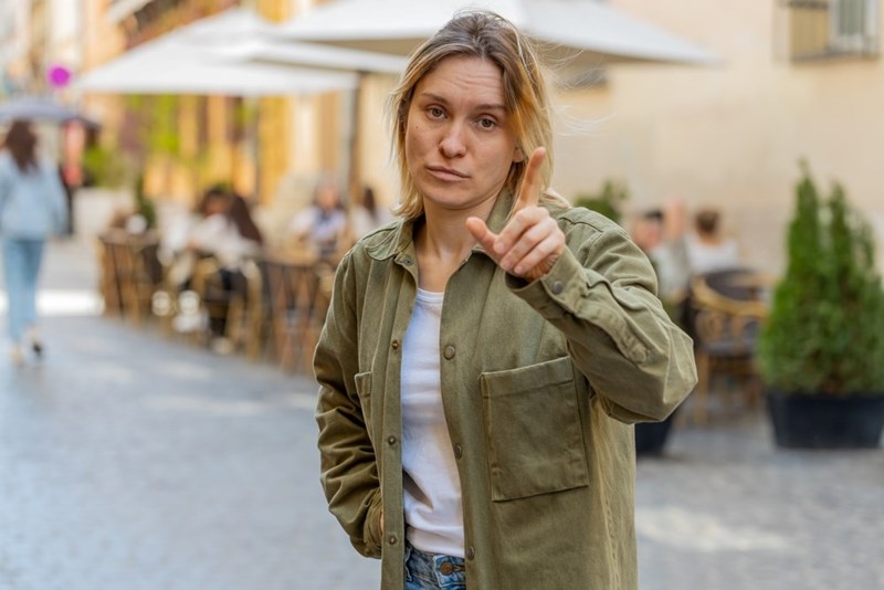 woman points towards camera with a firm, angry, unimpressed expression