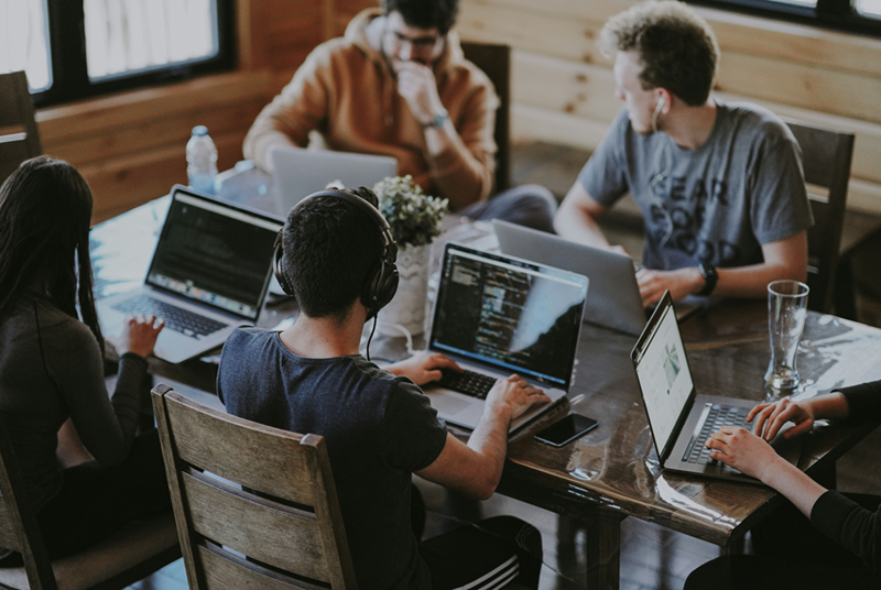 A group of startup employees sit around a conference table with laptops