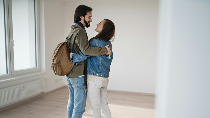 A man and a woman smile and hug one another in an empty room.