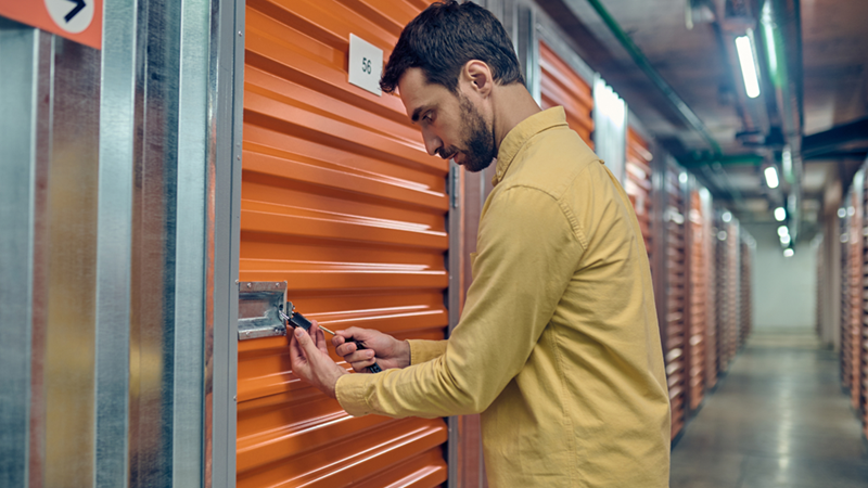 Man standing in a storage facility hallway trying to unlock a storage unit