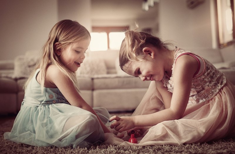 Two five-year-old twins sit on the ground painting each other's nails