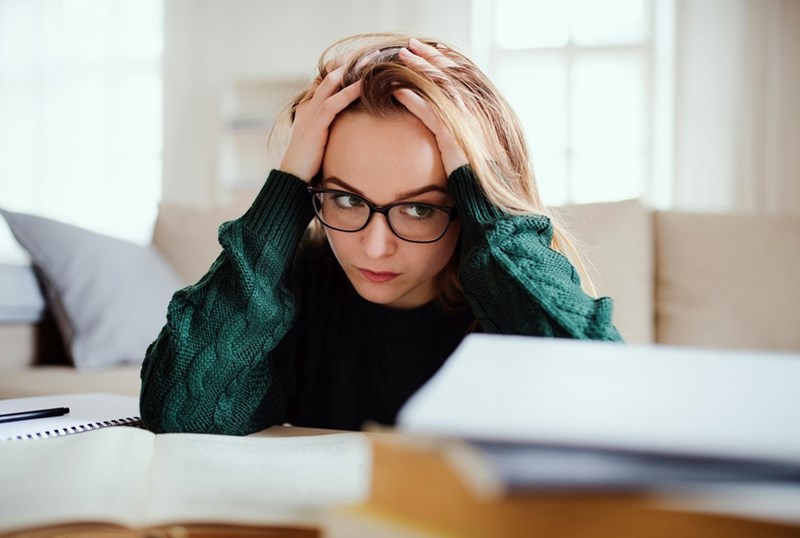 A frustrated young woman sits with books around her.