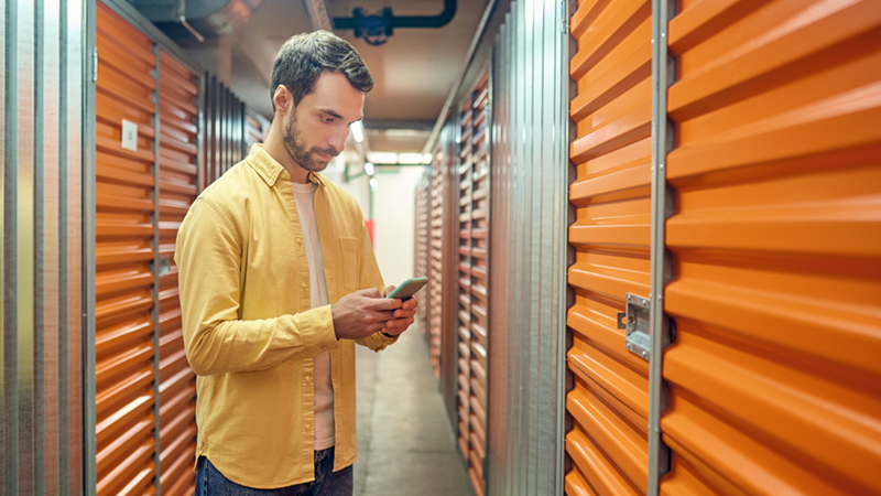 man looking at his smartphone standing in a self storage facility hallway
