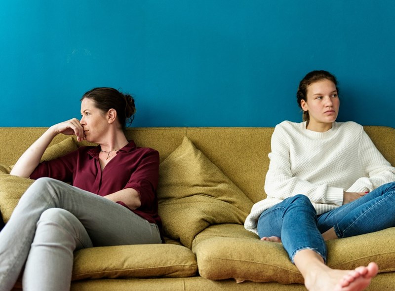 A young woman and her older relative sit angrily on the couch together