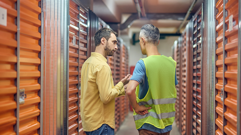 A customer and a storage facility worker discussing having a tense conversation in a storage facility hallway