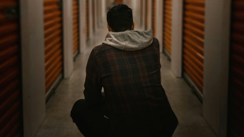 Man squatting in a dim lit storage facility hallway, signaling despair