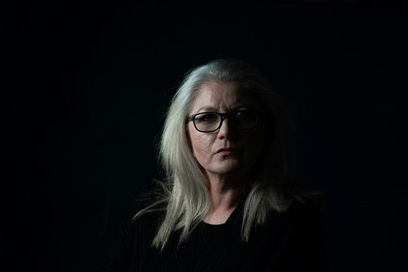 An older, sharply dressed but severe-looking woman against a shadowy background, representing the mother and her behaviour in the story.