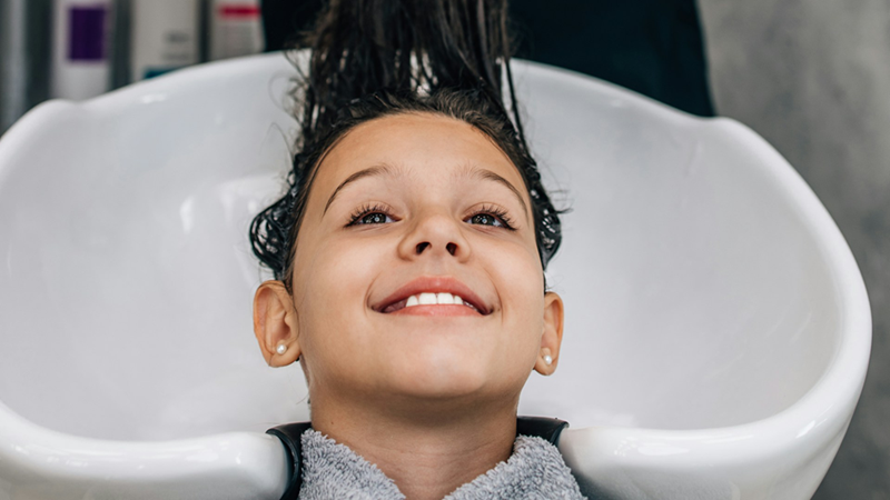 A young girl gets her hair washed in a sink at a hair salon.