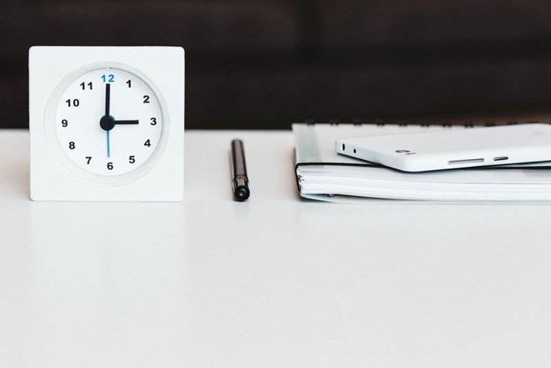 A white clock near a stack of papers on a desk