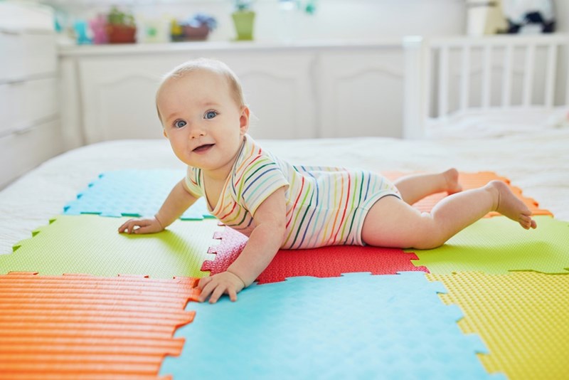 Happy smiling baby girl lying on colorful play mat on the floor.