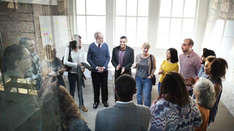 Large group of employess packed into a tight office space, pictured through a glass wall
