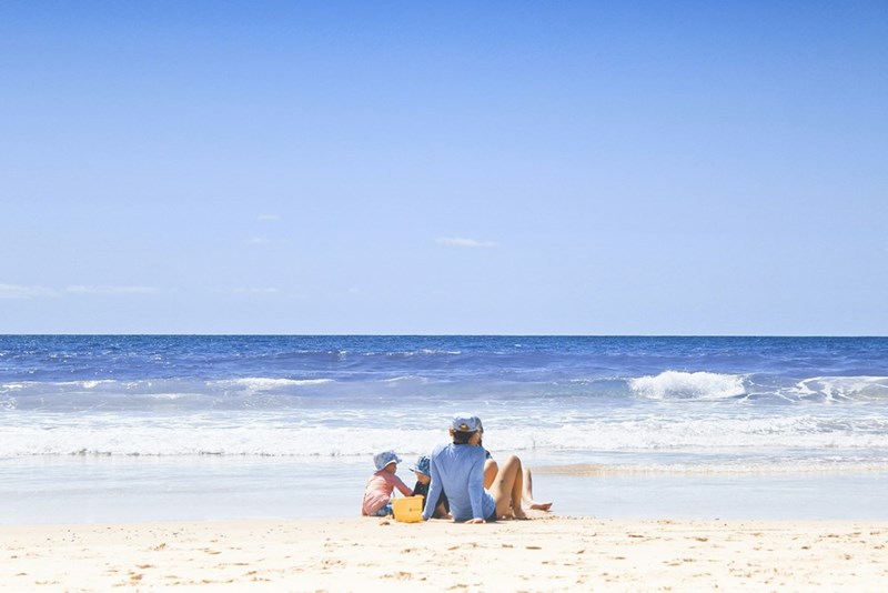 A parent relaxes on the beach with two young children during a family vacation to Mexico.
