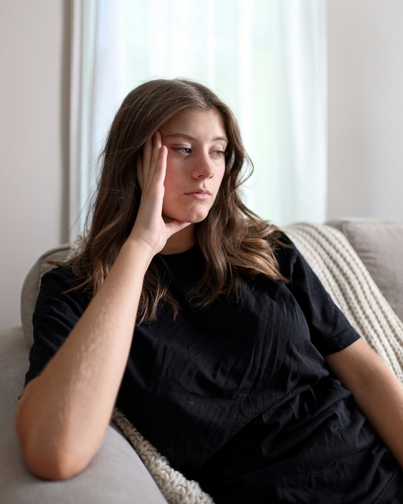 A frustrated young woman sits alone at home, thinking about the stress caused by her roommate using her bathroom.