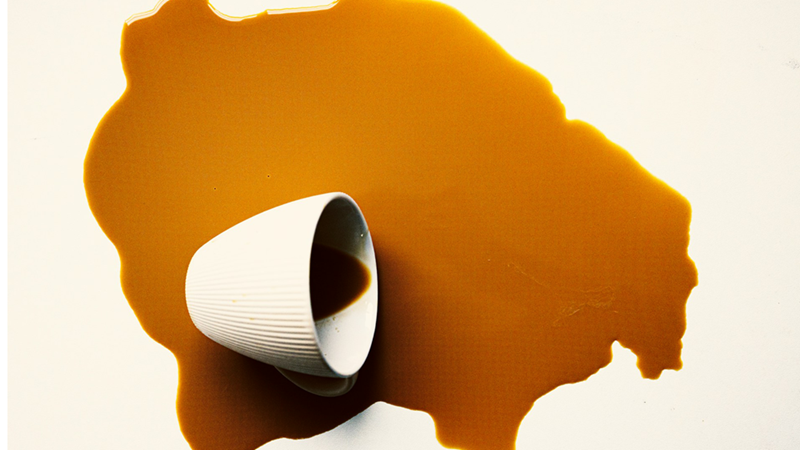 A cup of brown liquid spilt on a light-colored surface.