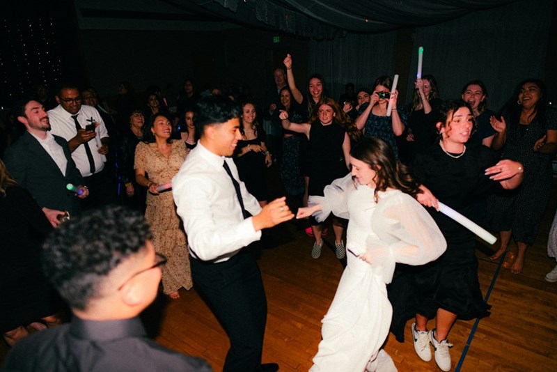 A wedding party dances on a dance floor, the bride and groom in center