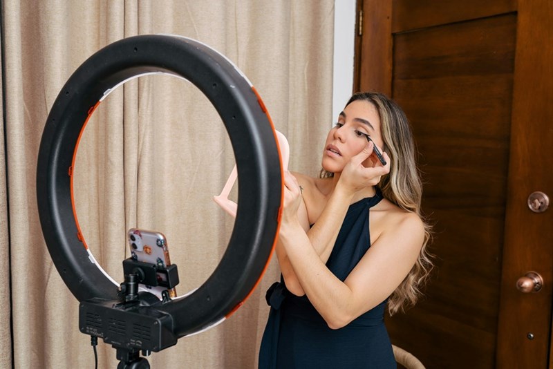 A content creator puts on makeup in front of a ring light
