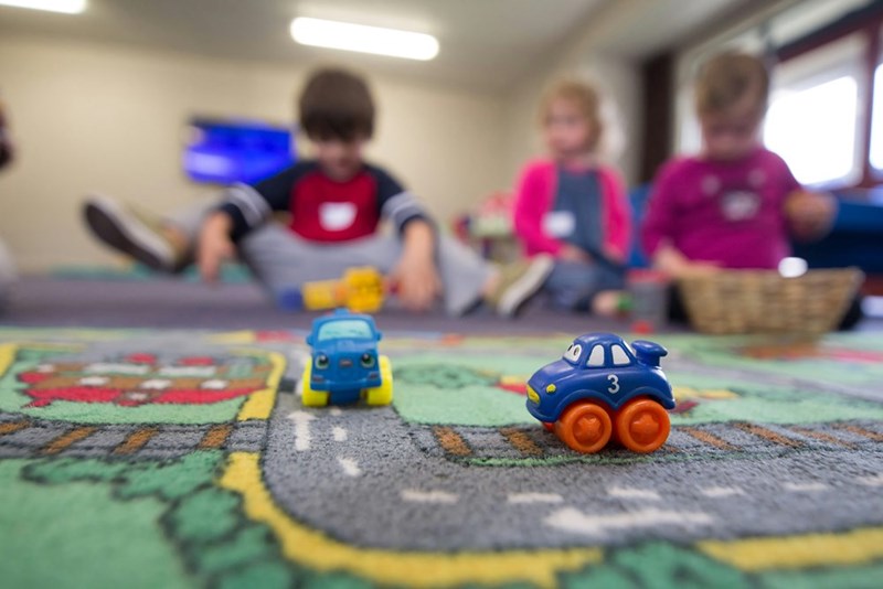 Kids playing with plastic car toys at daycare. Not actual story subjects.
