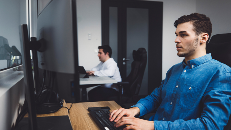 Two men working on separate computers in a small, tight office