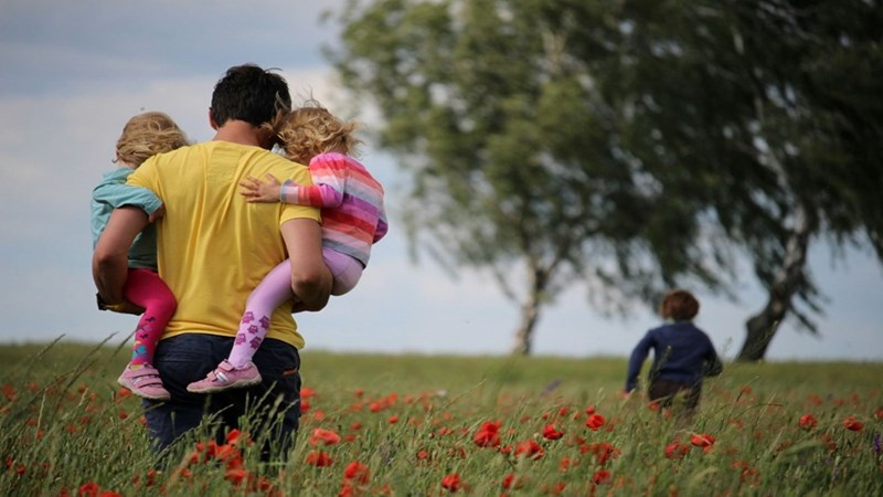 A dad carrying his children through the field. Still frame for contextual reference only. 
