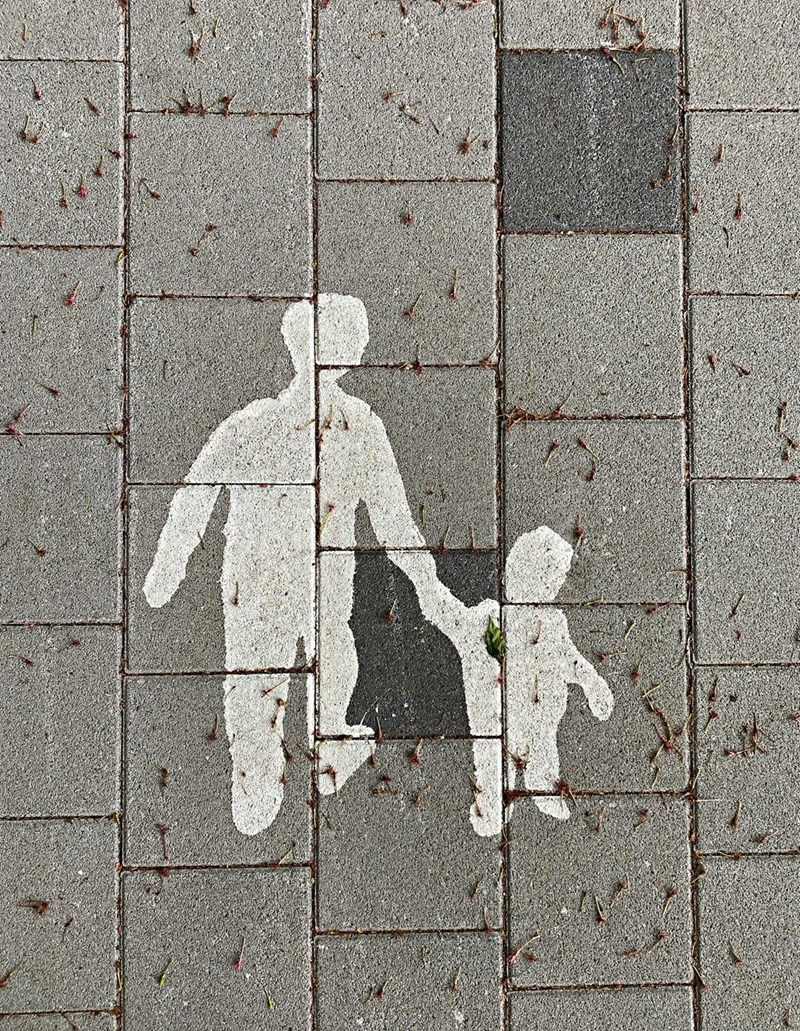 Two people walking on gray concrete pavement.