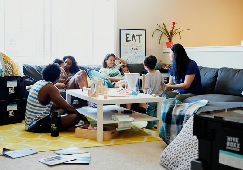 Roommates gathered in a shared living room, talking about the heat and what to do with the AC.