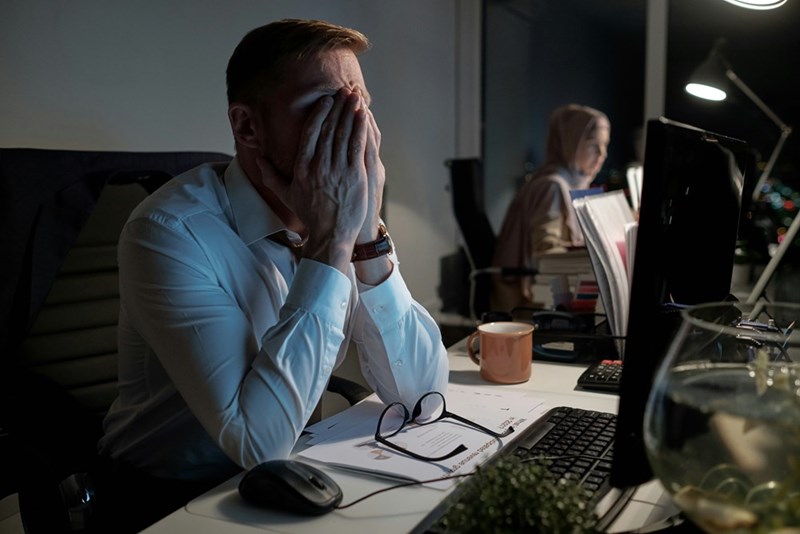 Exhausted office worker covering his face while working late.