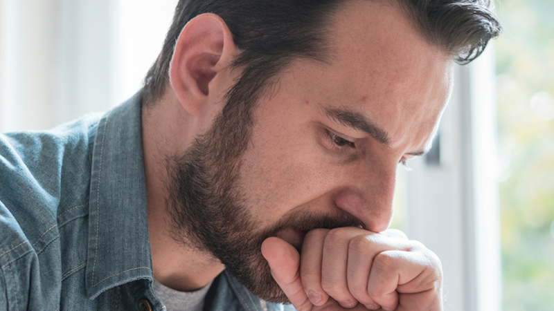 A man rests his mouth on his fist, looking worried.