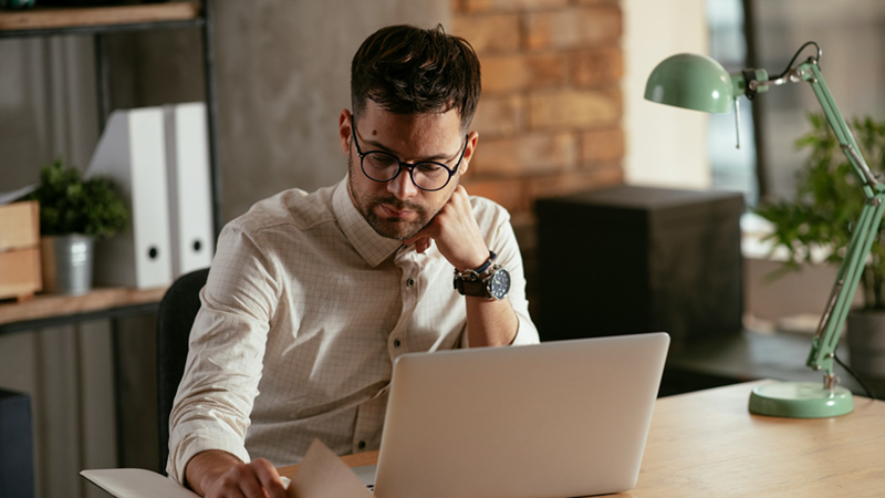 An employee rests his head on his fist as he works on his laptop.