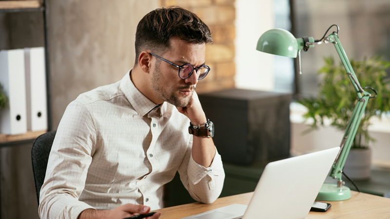 An employee rests his head on his fist as he works on his laptop.