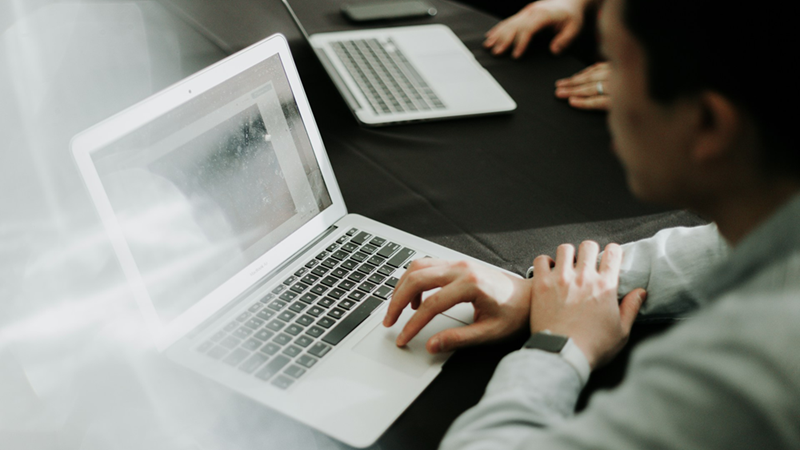 Side profile of a man using a laptop next to someone else using a laptop.
