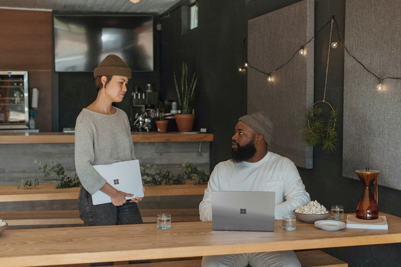 Two coworkers talk to each other at a communal table