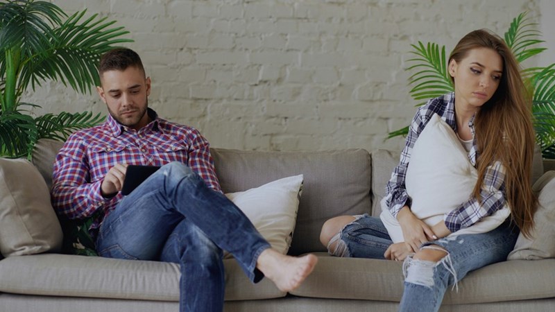 A couple look upset at each other while sitting on the couch