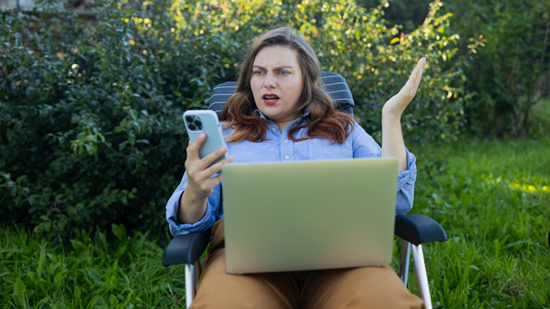 Woman sitting on a lounge chair reacting in disbelief to something on her phone