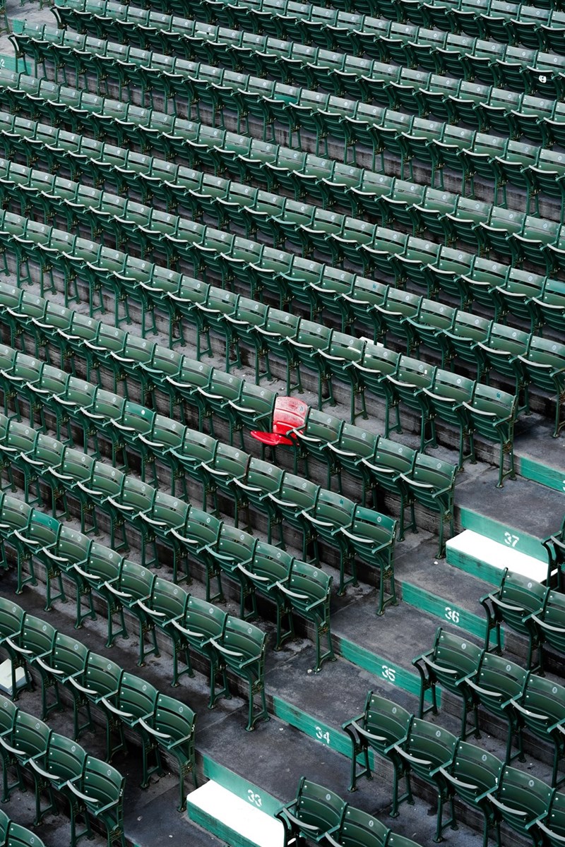 Rows of empty green stadium seats with one red seat