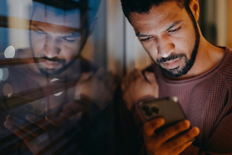A man looks stressed at his phone at night